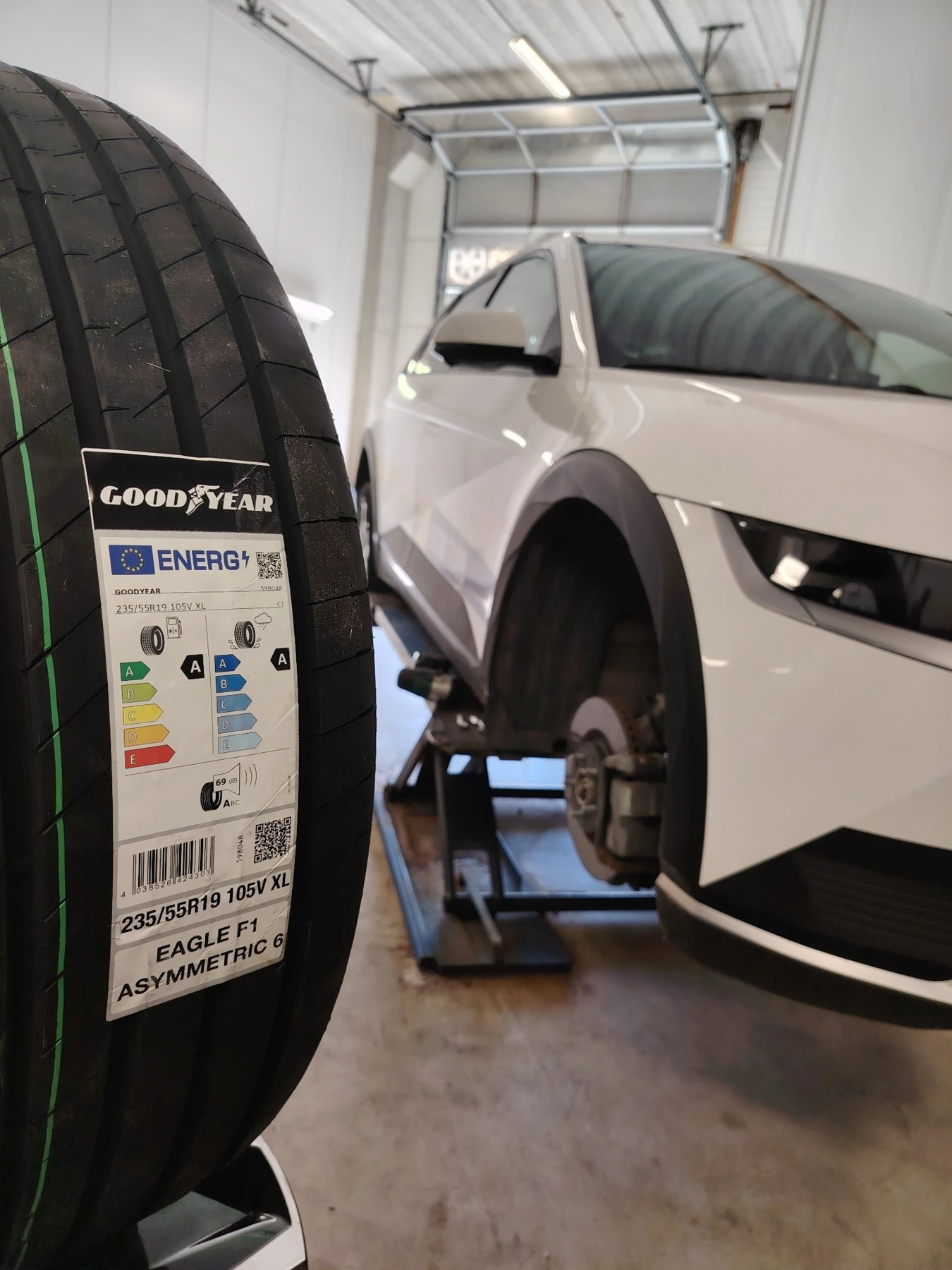Auto nosturilla rengastyössä ja Goodyear-rengas etualalla